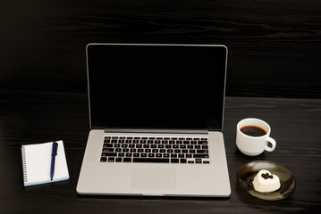 Open the laptop, mug of coffee, notepad and dessert on a black background
