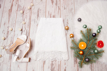 Lacy white skirt and white shoes on a wooden background, Christmas balls on fir branch. Fashionable concept, top view