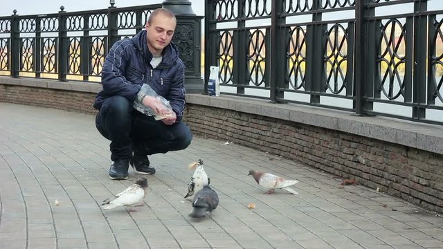 Young man feeding pigeons on the bridge.