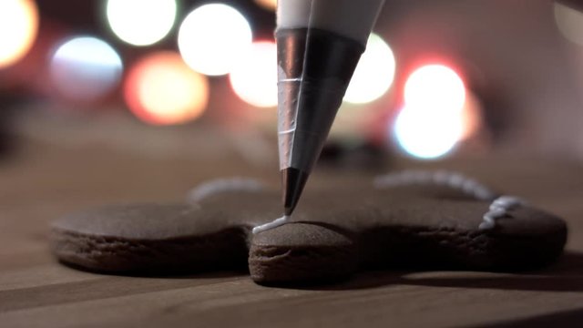 Female hand decorate Gingerbread man cookie with food icing on the table, close up. Bokeh in backgound.