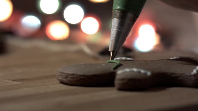 Female hand decorate Gingerbread man cookie with food icing on the table, close up. Bokeh in backgound.