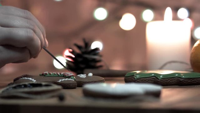 Female hand decorate Gingerbread man cookie with food icing on the table, close up. Bokeh in backgound.