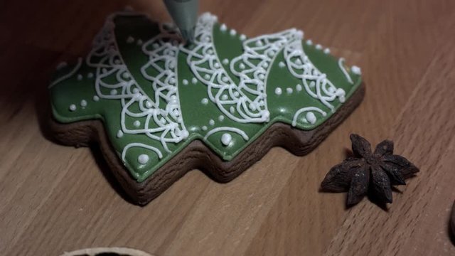 Female hand decorate Gingerbread green tree cookie with food icing on the table, close up.