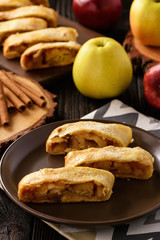Apple strudel with cinnamon on wooden background.
