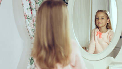 Fashionable little lady combing her hair and looking in the mirror
