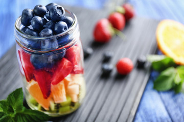 Glass jar with fruits and berries on wooden background