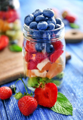 Glass jar with fruits and berries on wooden background