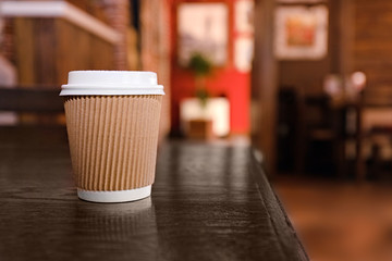 Paper cup with tasty coffee on wooden table in cafe, close up view