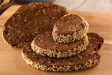 Sliced rye bread with seeds and sesame on wooden cutting board closeup