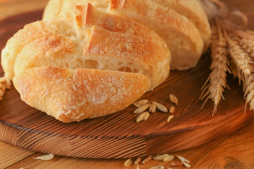 Sliced fresh bread with wheat spikes on wooden cutting board closeup