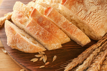 Sliced fresh bread with wheat spikes on wooden cutting board closeup