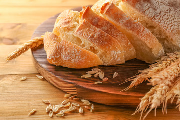 Sliced fresh bread with wheat spikes on wooden cutting board closeup