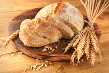 Sliced fresh bread with wheat spikes on wooden background