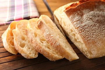 Slicing of fresh bread on wooden cutting board closeup