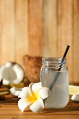 Mason jar with coconut water and beautiful plumeria flower on wooden background