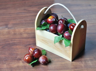 Plums with leaves in wooden box.