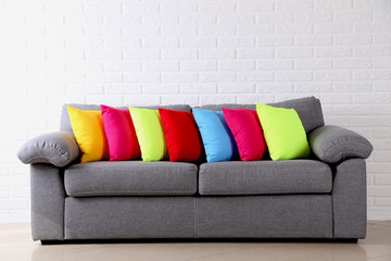 Colorful pillows on grey sofa on a brick wall background
