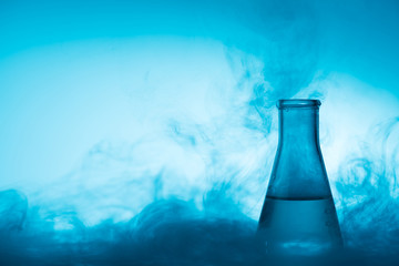 Chemical glass test tube with liquid and steam or smoke backlight on blue background with copy space