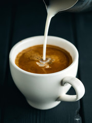 Milk pouring into cup of coffee