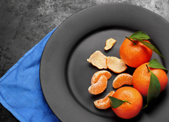 Ripe orange tangerines with green leaves on black ,matt plate , top view. Concept of healthy nutrition, diet, detox. Selective focus copy space