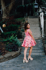 Beautiful brunette girl posing in pink dress outside near tropical plants