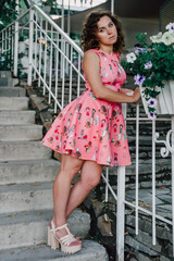 Beautiful brunette girl posing in pink dress outside near tropical plants