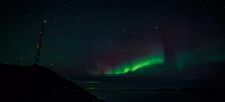 Radio tower on the hill and northern lights over the fjord in th
