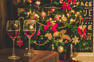 Two glasses with red wine on table. Blurred Christmas tree and fireplace in background.