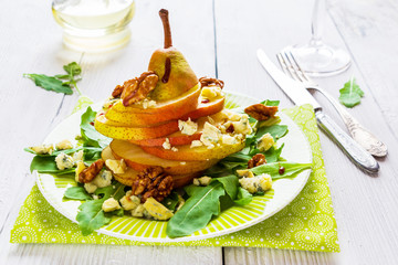 Fruit salad, whole pear sliced,  walnuts caramelized in honey, blue cheese and arugula. Green plate on wooden table, vintage knife and fork, horizontal photo.