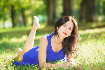 Beautiful young woman in blue dress lying on the grass