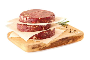 Wooden chopping board with stack of raw beef burger patties on white