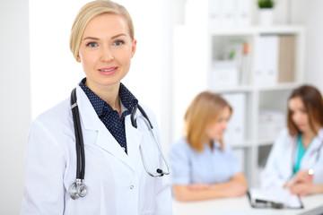 Female doctor smiling on the background with patient and his physician in hospital