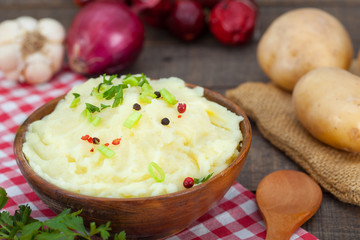 Homemade mashed potato with red and black peppers in wooden bowl. Fresh potatoes, onion, parsley and garlic on rustic table.