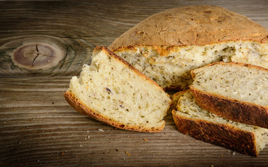 Sliced loaf of homemade bread made with herbs and spices on wooden background.