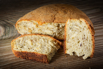 Sliced loaf of homemade bread made with herbs and spices on wooden background.