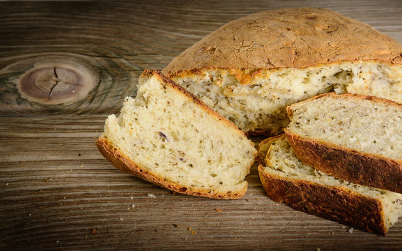 Sliced loaf of homemade bread made with herbs and spices on wooden background.