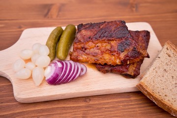 Barbeque pork spare ribs marinated in mustard, honey and chili, served on the wooden plate with pickled baby onions, cucumbers and fresh red onion. Side dish is a wholegrain bread. Simple delicious. 