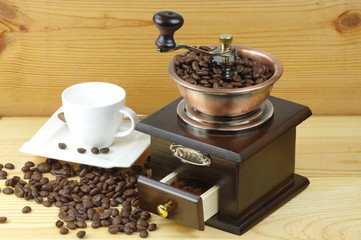 Old-style manual coffee grinder on a rustic table with wooden planks. Around the mill are scattered...