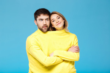 Couple in yellow sweater posing with crossed arms over blue background.
