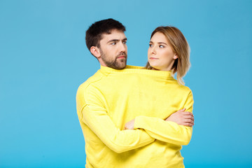 Couple in yellow sweater posing with crossed arms over blue background.