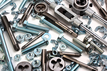 Many shiny bolts with nuts, taps and dies on white background