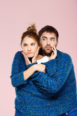 Young beautiful couple in one blue knitted sweater posing smiling having fun over light pink background.