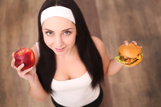 Young attractive girl making choice between healthy and harmful food