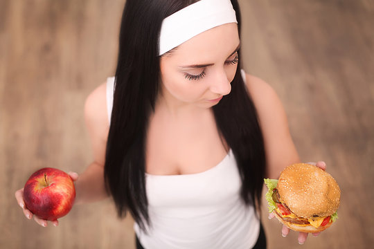 Young beautiful asian girl making choice between hamburger and a red apple, healthy eating and lifestyle concept.