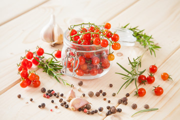 tomatoes in a jar, rosemary and garlic on a wooden background, selective focus