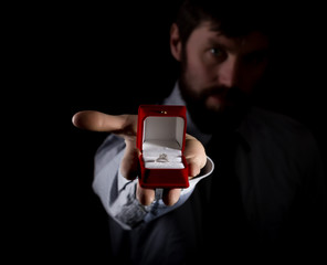 bearded man in business suit gives a ring in the red box and expresses different emotions on dark background