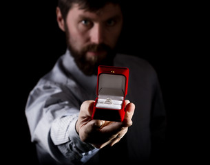 bearded man in business suit gives a ring in the red box and expresses different emotions on dark background