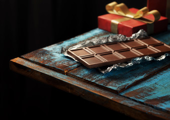 Bar of milk chocolate and red gift box wooden table