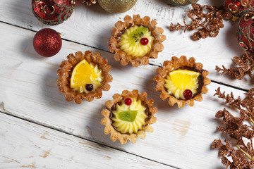 Homemade desserts with fruits for the new year. Desserts for the holidays. View from above. Christmas decorations and toys. The desserts on the wooden background.