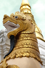 Fototapeta na wymiar GOLDEN LION AND GOLDEN PAGODA Golden lion statue stand still in front of golden pagoda as a guard to protect the sacred place.